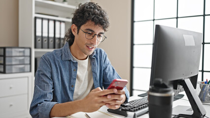Young hispanic man business worker using smartphone smiling at office