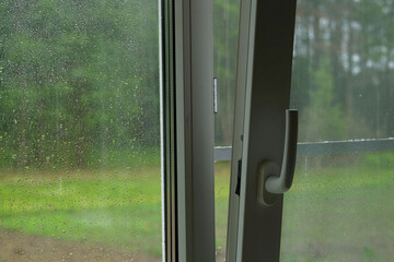 Raindrops on a window pane. Rain drops on transparent glass on a green background. Soft focus. Concept of sadness, bad mood, Wet. Gray sky. Rainy summer weather. Close Up view of droplet of water