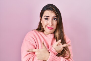 Young hispanic woman standing over pink background pointing to both sides with fingers, different direction disagree