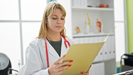 Young blonde woman doctor reading medical report at clinic