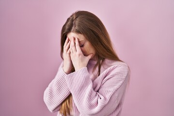 Young caucasian woman standing over pink background with sad expression covering face with hands while crying. depression concept.