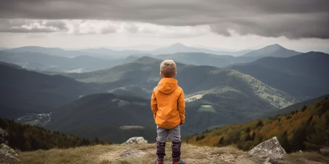 Fotobehang A young child hiker stares out of a scenic mountain view, large hilly landscape, orange coat jacket © Nick