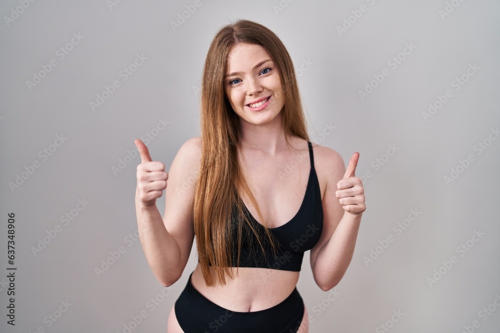 Sticker Young caucasian woman wearing lingerie success sign doing positive gesture with hand, thumbs up smiling and happy. cheerful expression and winner gesture.