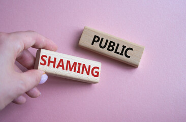 Obraz premium Public Shaming symbol. Concept word Public Shaming on wooden blocks. Businessman hand. Beautiful pink background. Business and Public Shaming concept. Copy space