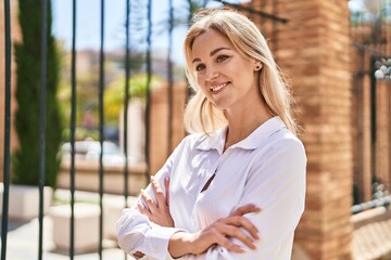 Young blonde woman smiling confident standing with arms crossed gesture at street