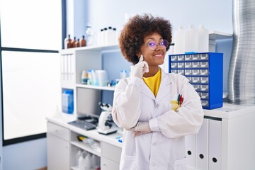 Young african american woman working at scientist laboratory smiling looking confident at the camera with crossed arms and hand on chin. thinking positive.
