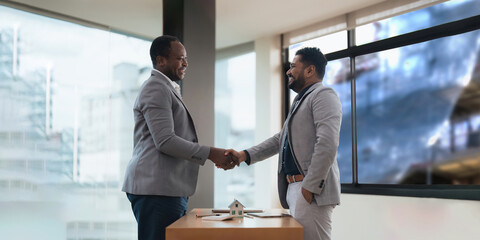 Real estate agents African American and customers indian shake hands to congratulate on signing a contract to buy a house with land