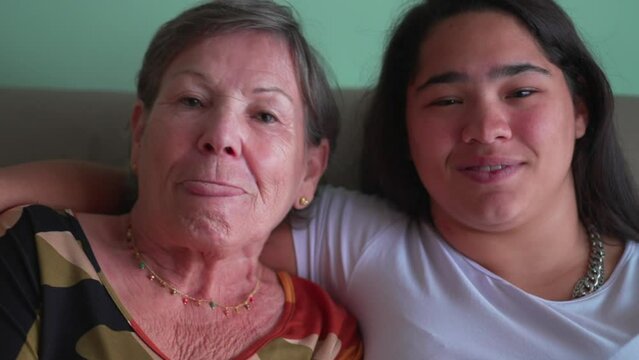 Happy ethnically diverse inter generation granddaughter and grandmother posing for camera together. Grandchild kissing grandparent on the cheek