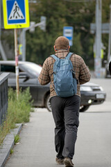 A man with a backpack walks along the sidewalk on a summer day