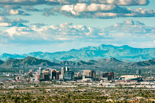 The skyscrapers of Phoenix, Arizona against mountains and a cloud-filled sky.