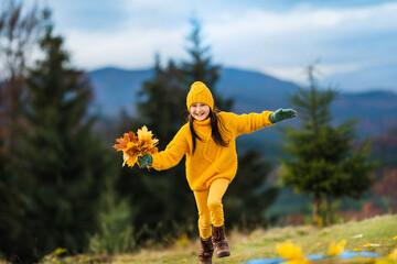 A small child runs with a bouquet of yellow maple leaves in his hands.
