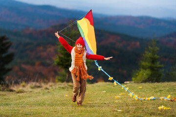 Small happy child runs and plays with kite in the autumn season. Bouquet of yellow maple leaves in...