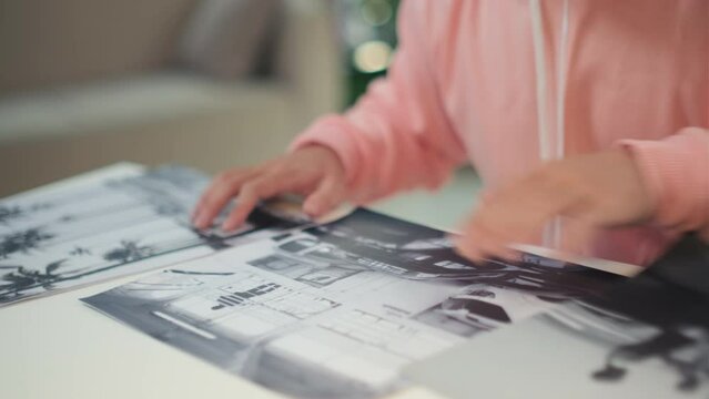 Cropped shot of man in pink hoodie choosing black and white pictures for exhibition in art gallery while sitting at table
