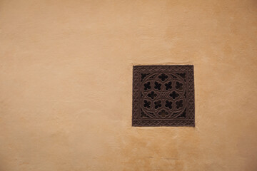 Yellow Roman wall texture background, Italy. Ventilation hole  on the shabby yellow wall facade. Old european house background. Ornamental ventilation hole in an ochre colored stone wall.