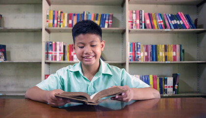 At the library, a young boy of Asian descent is deeply engrossed in reading a book during his break.