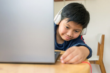 Asian cute kid boy reaches out to plug his headphones into his laptop by himself with a face that intends to use the computer to study online at home. link and connect