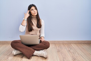 Young brunette woman working using computer laptop sitting on the floor shooting and killing oneself pointing hand and fingers to head like gun, suicide gesture.