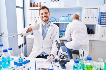 Hispanic man and woman working at scientist laboratory smiling happy and positive, thumb up doing excellent and approval sign