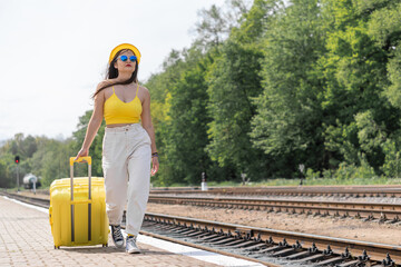 A world of vivid impressions awaits: a young woman in sunglasses and stylish clothes is ready to go on a journey. A fun and energetic journey: a girl in a bright stylish outfit is ready to discover