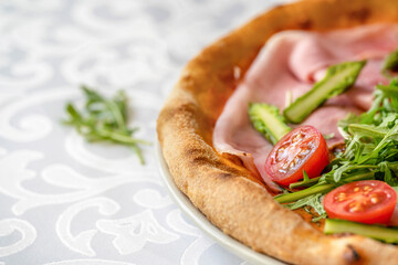 Detail of a tasty ham pizza with fresh tomato, arugula and asparagus on the restaurant table.