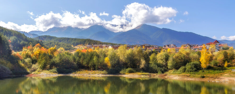 Bansko, Bulgaria autumn banner panorama background of Pirin mountain peaks, Krinets lake water, colorful green, red and yellow trees reflection