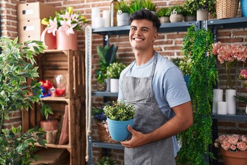 Young hispanic man florist smiling confident holding plant at flower shop