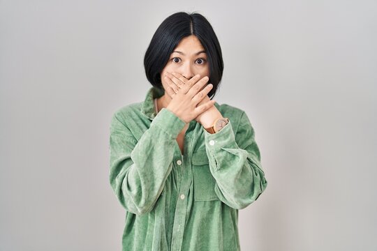 Young asian woman standing over white background shocked covering mouth with hands for mistake. secret concept.