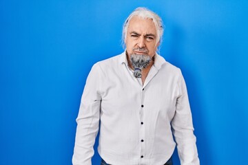 Middle age man with grey hair standing over blue background skeptic and nervous, frowning upset...