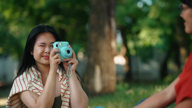 Confident asian woman taking pictures on camera of her friend outdoors