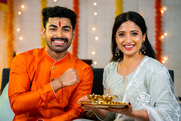 Happy smiling indian brother showing rakhi with sister by looking at camera at home - concept of family relationship, tradition ceremony and indian culture.