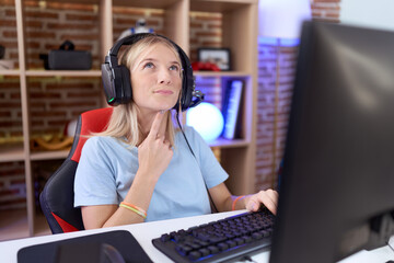 Young caucasian woman playing video games wearing headphones thinking concentrated about doubt with...