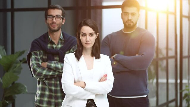three colleagues stand in the lobby of a modern office with their arms crossed