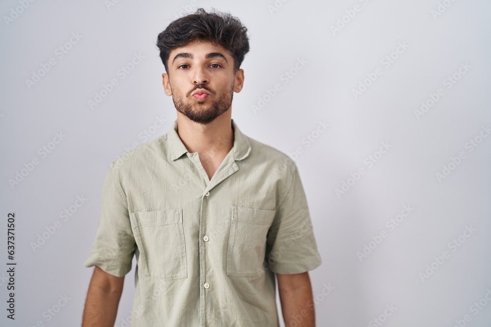 Sticker Arab man with beard standing over white background looking at the camera blowing a kiss on air being lovely and sexy. love expression.