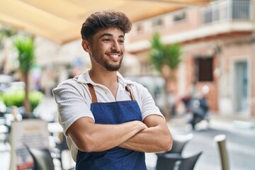 Young arab man waiter standing with arms crossed gesture at restaurant