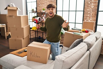 Arab man with beard moving to a new home closing cardboard box celebrating achievement with happy smile and winner expression with raised hand