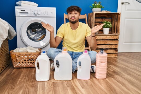 Arab man with beard doing laundry sitting on the floor with detergent bottle shouting and screaming loud to side with hand on mouth. communication concept.