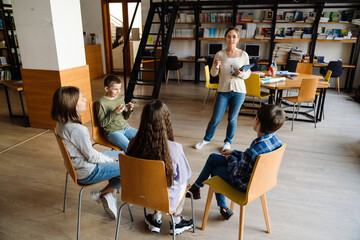 Female school teacher teaching group of children in library
