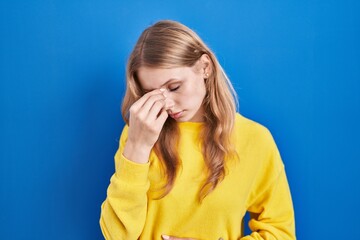 Young caucasian woman standing over blue background tired rubbing nose and eyes feeling fatigue and headache. stress and frustration concept.