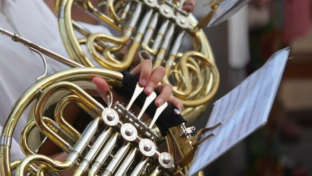 During a parade, a musician's trombone playing is showcased, zooming in on the instrument and hands. Filmed slowly.