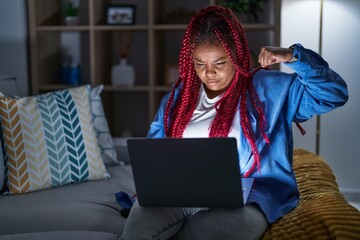 African american woman with braided hair using computer laptop at night strong person showing arm muscle, confident and proud of power