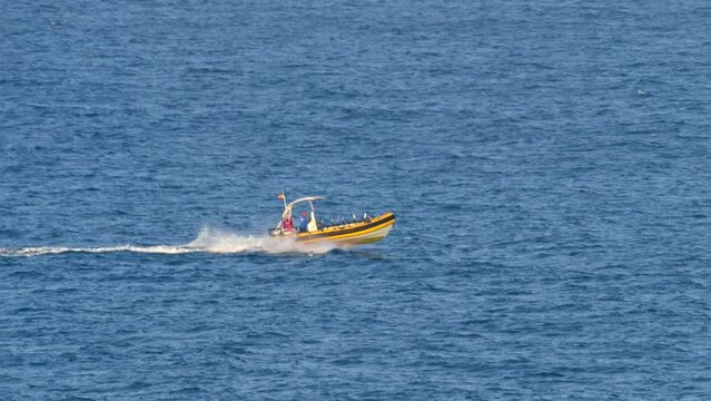 Motorized boat in yellow and red colors, equipped with a shade, moves across slightly turbulent sea waters.