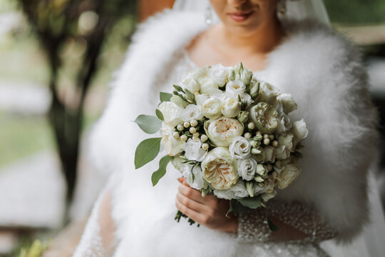 A beautiful queen with a bouquet of flowers in her hands. Charming woman bride is walking in the park. A wedding outfit, a lush dress, a luxurious cloak, a white cape made of swan feathers.