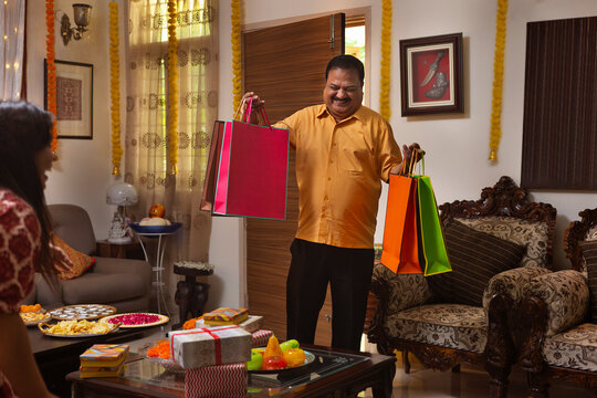 man is happily entering the house with gifts and shopping bags for his family, during the festival of Diwali 