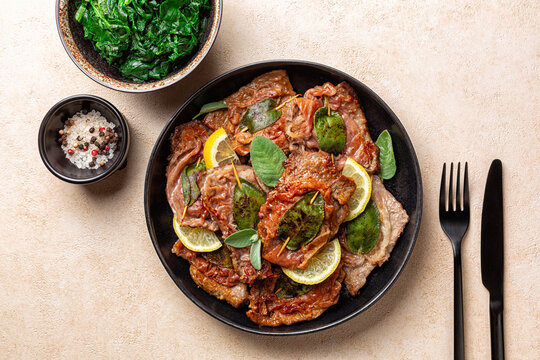 Top view of italian Roman dinner. Saltimbocca alla Romana, Italian dish. It consists of veal or beef, that has been cooked with prosciutto ham and sage and then cooked in wine. Sauteed Spinach.