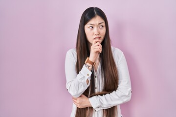 Chinese young woman standing over pink background thinking worried about a question, concerned and nervous with hand on chin