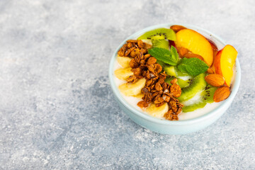 Bowl of granola with yogurt and fresh berries on a texture table. Yogurt berries, acai bowl, spirulina bowl. Healthy food, balanced breakfast. Strawberries, blueberries, kiwi, peach, almonds and chia.