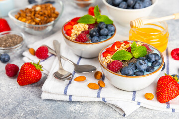 Bowl of granola with yogurt and fresh berries on a texture table. Yogurt berries, acai bowl, spirulina bowl. Healthy food, balanced breakfast. Strawberries, blueberries, kiwi, peach, almonds and chia.