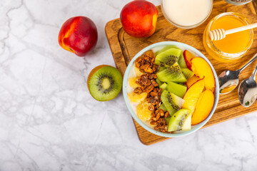 Bowl of granola with yogurt and fresh berries on a texture table. Yogurt berries, acai bowl, spirulina bowl. Healthy food, balanced breakfast. Strawberries, blueberries, kiwi, peach, almonds and chia.