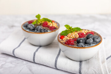 Bowl of granola with yogurt and fresh berries on a texture table. Yogurt berries, acai bowl, spirulina bowl. Healthy food, balanced breakfast. Strawberries, blueberries, kiwi, peach, almonds and chia.