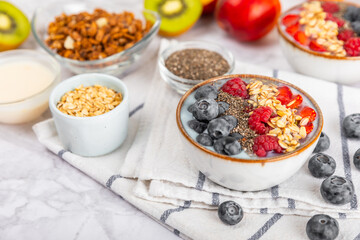 Bowl of granola with yogurt and fresh berries on a texture table. Yogurt berries, acai bowl, spirulina bowl. Healthy food, balanced breakfast. Strawberries, blueberries, kiwi, peach, almonds and chia.
